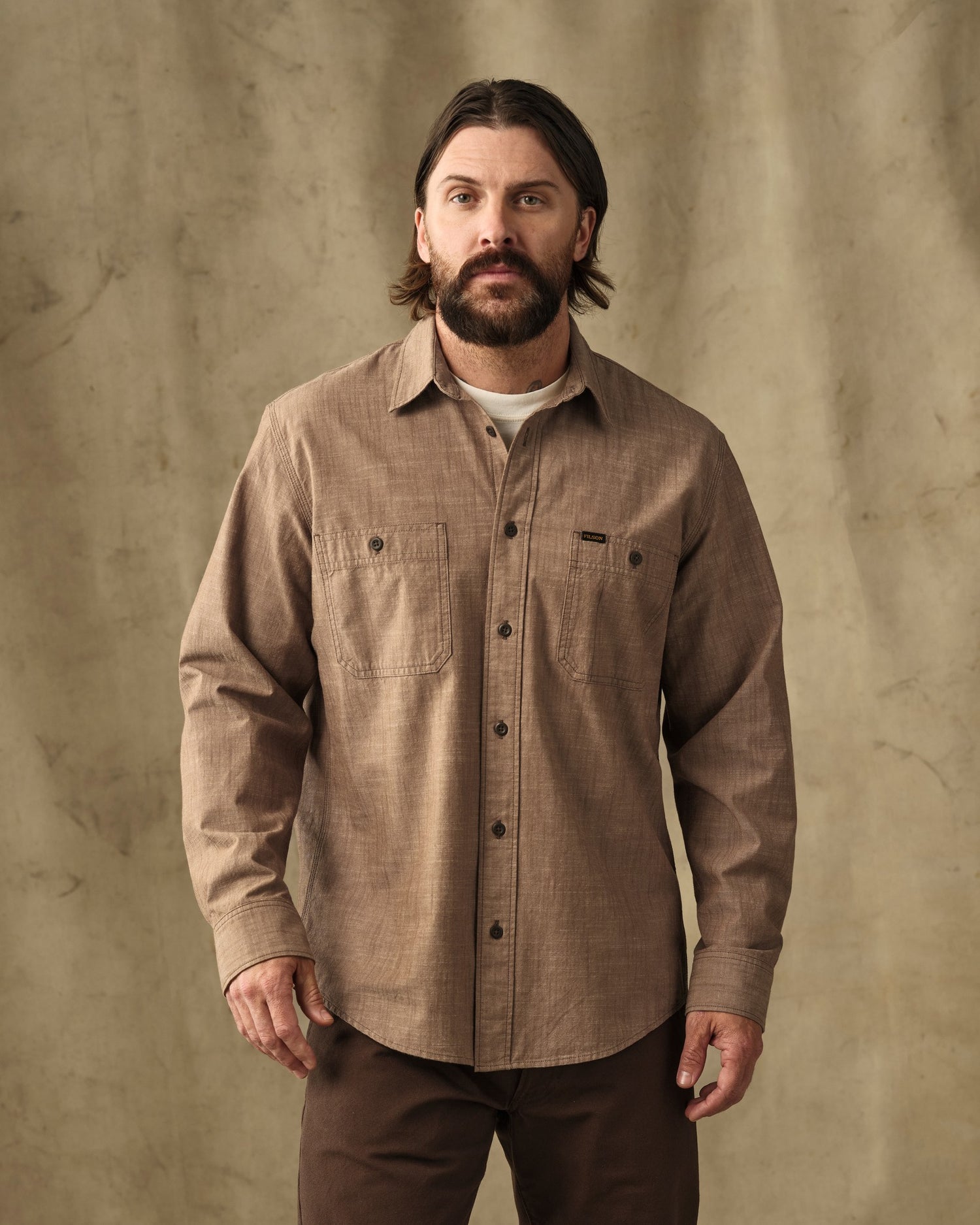 image of a model wearing Filson's Chambray CPO Shirt - Dark Tan|Model is 6' wearing a size medium